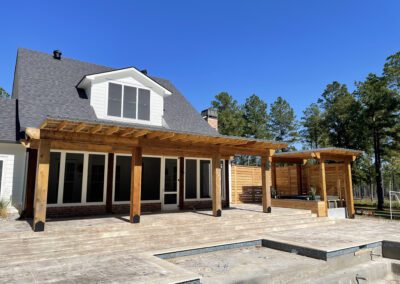 A home with a covered patio and a deck, surrounded by lush greenery.