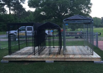 An outdoor dog kennel enclosed by a fence, featuring a wooden bench.