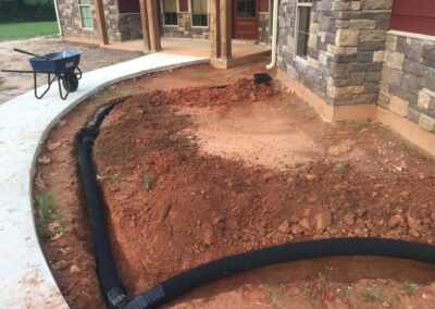 A dirt driveway leading to a house with a small garden in the front yard.