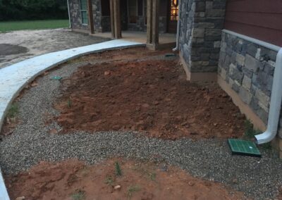 A dirt driveway leading to a house with a small garden in the front yard.