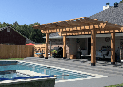 A pool surrounded by a patio and a wooden pergola.